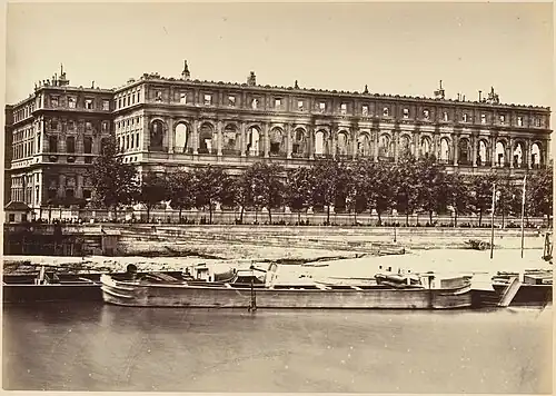 Au premier plan un fleuve. A l'arrière plan un grand bâtiment rectangulaire gris dont il ne reste que les façades.