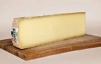 photo couleur d'une tranche de fromage couleur ivoire sur une planche en bois. La morge est plus sombre.