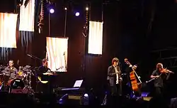 Denez Prigent chantant sur scène accompagné de ses musiciens.