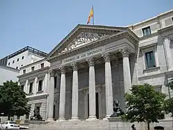 Photographie d'un bâtiment public, avec six colonnes doriques en façade et le drapeau espagnol sur le toit.
