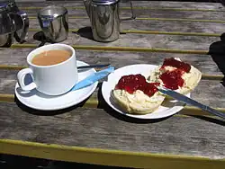 Vue d'une tasse de thé et de deux moitiés d'un scone préparés selon la méthode du Devon dans une assiette.