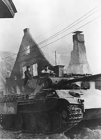 Char d'assaut devant les ruines d'une maison