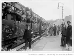 Photographie de plusieurs voitures remplies de conscrits en train de quitter le quai.