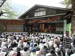 Photo couleur montrant des spectateurs assis devant une scène ouverte sur laquelle se joue une pièce de kabuki.