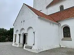 Église en pierre blanche aux tuiles rouges, atmosphère paisible, centrée sur l'entrée et les fenêtres vertes.