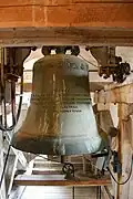Cloche en bronze vert-brun suspendue dans un clocher en bois, ambiance solennelle.
