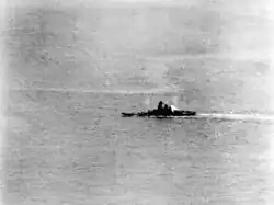 Photographie en noir et blanc d'un bateau qui gîte sur la bâbord. De la fumée est visible.