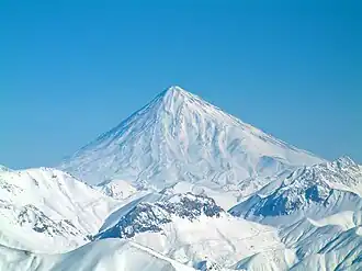 Volcan conique, enneigé, surmontant très largement des montagnes d'altitude plus modeste, bien qu'également enneigées.