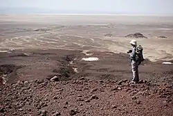 Paysage de la dépression de Danakil. Les roches de couleurs blanches au second plans sont des sédiments marins. L'Erta Ale est visible en arrière-plan.
