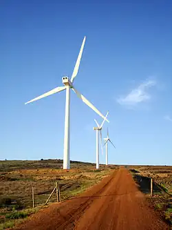 Trois éoliennes au bord d'une route terreuse.
