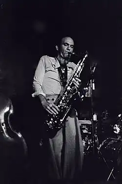 photo noir et blanc d'un homme sur scène, en train de jouer du saxophone