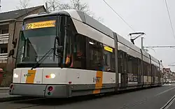 La photo couleur montre une rame grise en blanche rayée de jaune-orangé dans une rue pavée.