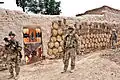 Des soldats américains patrouillant devant un qalat&nbsp;(en) afghan couvert de bouses de vache façonnées et séchées, en Afghanistan.