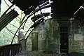 Intérieur de la cabane abandonnée de Nissen ; les tôles ondulées formant les murs et le toit sont soutenues par des cloisons de séparation en briques et des poutres métalliques.
