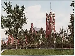 Carte postale en photochromie d'un bâtiment aux façades rouges dont une partie est recouverte de végétation.