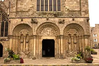 Photographie d'un bas de façade d'église avec trois arcades romanes.
