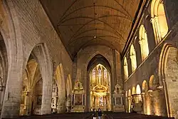 Photographie d'une nef d'église prise en direction du chœur, avec un mur à droite et des arcades à gauche.