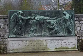 Surmonté d'un bas-relief en bronze, la scène représente un gisant qu'un ange vient coiffer d'une couronne. Un second personnage à droite tend également une couronne à la veuve éplorée tenant son enfant qui est agenouillée au pied du défunt. Le socle mentionne le souvenir dinantais aux 674 victimes innocentes de la furie teutonne dont 116 trouvèrent la mort ici.