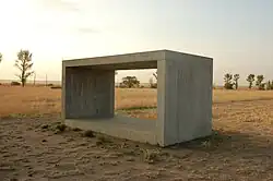 dans une plaine aride, un gros bloc de béton évidé, qui permet de voir à travers, comme une fenêtre.