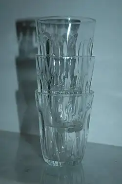 Photographie en couleurs de face, de trois verres de table empilés l'un dans l'autre, sur une table.