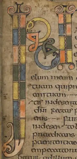 Initiale médiévale ornée de motifs colorés, de style miniature, sur fond clair. Éclairage diffus, détails précis, texte médiéval. Atmosphère d'ouvrage ancien.
