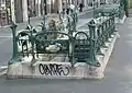 Photo en couleurs d'un entourage à cartouches ajouré vu du côté carré opposé à l'escalier et dont le socle en pierre s'orne de quelques tags