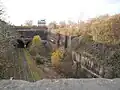 Tranchée ferroviaire abandonnée et recouverte par la végétation menant à trois tunnels, eux aussi abandonnés.