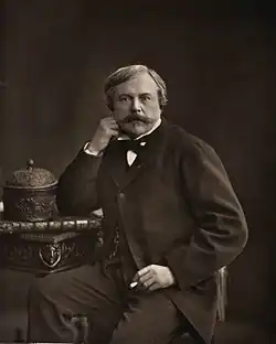 Portrait photographique d'un homme assis sur une chaise, le poing droit appuyé sur son visage.