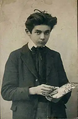 Photo noir et blanc en plan américain d'un adolescent à l'air sérieux, en costume sombre, palette à la main