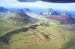 Vue aérienne de Heimaey avec l'Helgafell (à gauche), l'Eldfell (à droite) et sa fissure volcanique au premier plan.