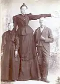 Photographie noir et blanc du père et de la mère de la géante qui sont présentés sous son bras tendu