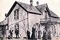 Photographie noir et blanc d'une maison à 1 étage dont les portes et fenêtres sont plus hautes et larges que les ouvertures classiques
