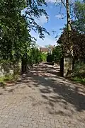 Photo d'un chemin conduisant à une maison cachée derrière des arbres. Un grand portail est ouvert et un panneau noir porte la mention « Abberton Hall » en lettres blanches