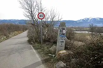 Vue d’une borne au bord d’une route, devant un panneau de limitation de vitesse.