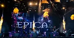Image montrant six membres d'un groupe de rock jouant sur une scène avec des effets pyrotechniques
