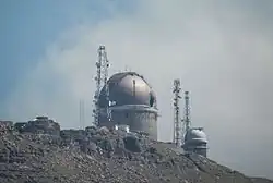 Photo d'un observatoire sur une montagne, avec un ciel nuageux.