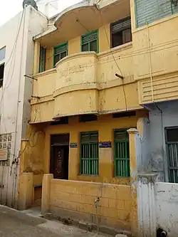 Photo couleur d'une façade jaune d'une maison à deux étages présentant chacun deux fenêtres et une porte.