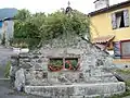 Un monument avec abreuvoir fleuri surmonter d'une croix.