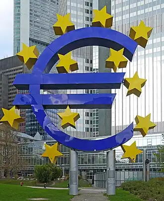 :Euro-Skulptur (en), monument représentant le symbole de l'euro entouré des étoiles du drapeau européen, devant l'Eurotower, ancien siège de la BCE, à Francfort-sur-le-Main.