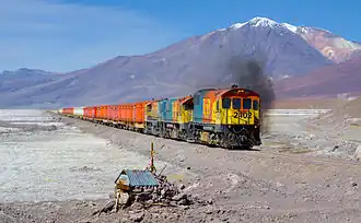 Un train du FCAB tracté par trois locomotives diesel EMD traverse le désert salé d'Acostan&nbsp;(en) (en espagnol salar de Ascotan) sur la ligne Ollagüe – Calama. En arrière-plan le stratovolcan "Cerro del Azufre" qui culmine à 5846 mètres.
