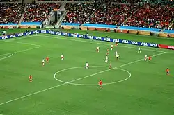 Photo d'un match de football entre une équipe jouant en blanc et l'autre en rouge vu depuis les tribunes