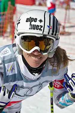 Portait de d'une skieuse, légèrement penchée en avant, avec un casque et des lunettez de ski.