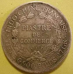Photographie d'une pièce de monnaie ancienne, portant les mentions « Indochine française » et « Piastre de commerce ».