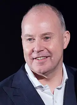 Un homme d'une quarantaine d'années, presque chauve, souriant.