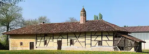 Un long bâtiment à colombages surmonté d'une cheminée sarrasine en brique rouge ressemblant à un clocheton.