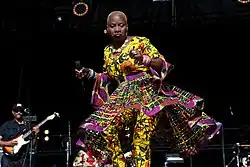 Femme africaine vêtue d'une robe jaune à volants en train de danser sur une scène de spectacle.