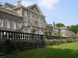 Photo d'une grande demeure élégante aux murs gris clair percés de nombreuses fenêtres. Une pelouse soigneusement entretenue est visible au premier plan.