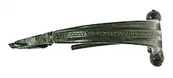 Fibule fragmentaire de couleur verte, ornée de motifs géométriques.
