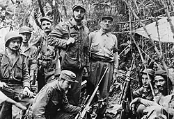Photo en noir et blanc d'un groupe d'hommes armés et en tenue militaire, dans la jungle.
