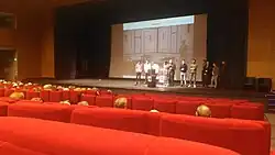 Photographie d'une salle de conférences avec un groupe de personnes sur l'estrade.